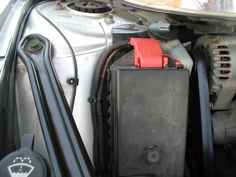 Car engine bay showing battery, fuse box, and alternator