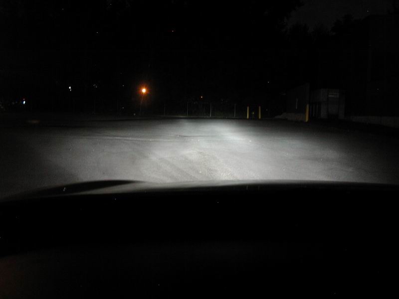 View from inside a vehicle at night, looking down a road illuminated by headlights