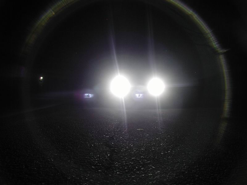 Car headlights on a dark road. The image has a lens flare effect