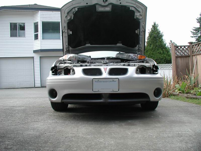 Front of a 2002 Pontiac Grand Prix with hood open, headlights removed, parked in driveway