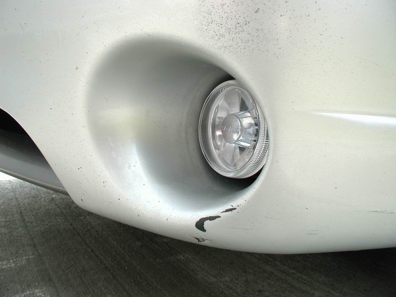 Close-up of a car's front bumper with a fog light assembly visible. Shows some scuff marks and paint chips
