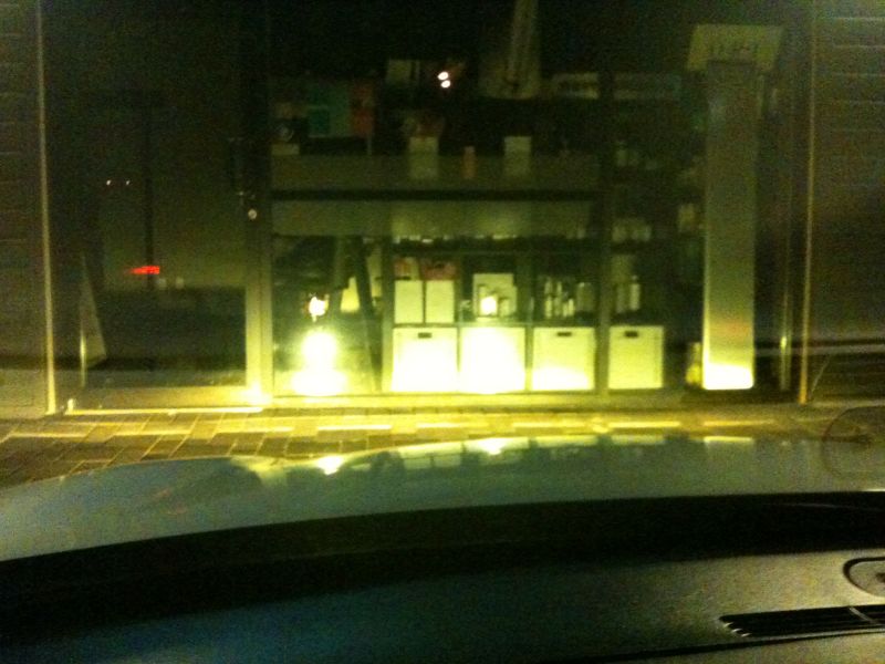 Night view over a car dashboard and hood toward a dimly lit storefront