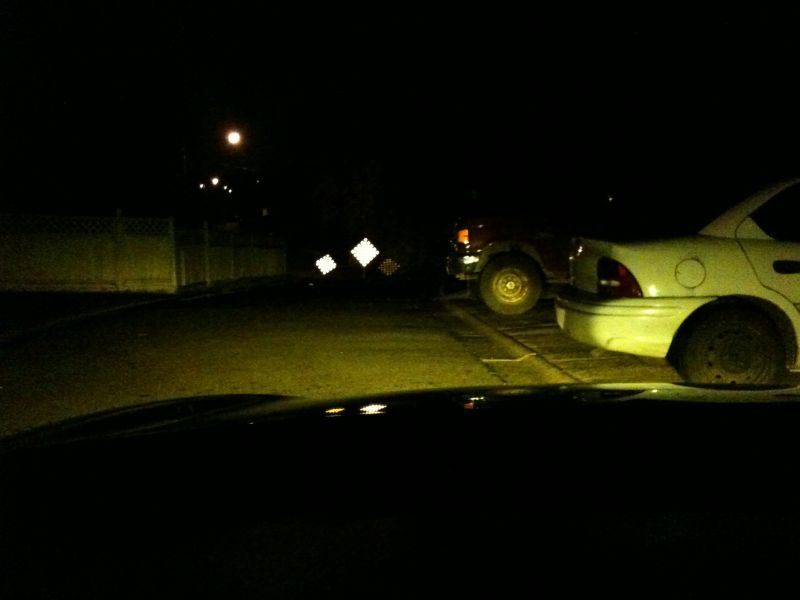 Night view from a car dashboard toward a parked sedan and pickup in a dark lot