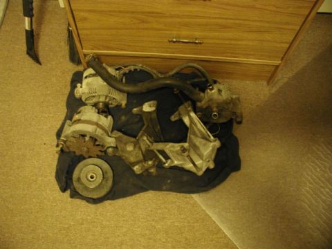 1990 Ford F-250 - Close-up of a disassembled alternator and mounting bracket, likely for a vehicle engine repair.
