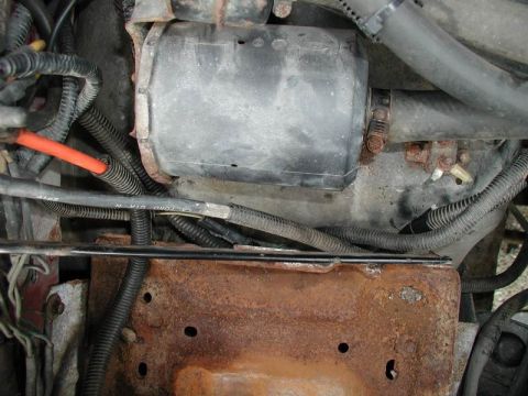 1990 Ford F-250 - Engine bay detail with various hoses, wiring, and a black component, showing signs of rust.