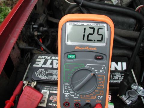 1990 Ford F-250 - A multimeter displays a voltage reading of 12.5V while connected to a car battery in an engine bay.