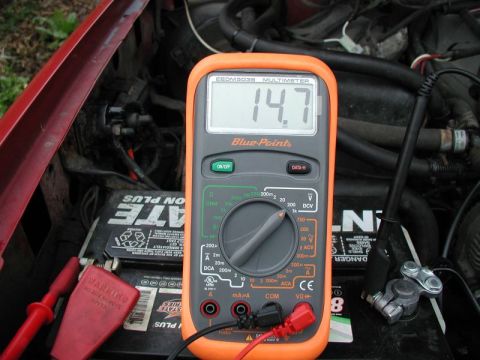 1990 Ford F-250 - A multimeter reads 14.7 volts while connected to a car battery, indicating the charging system is functioning.