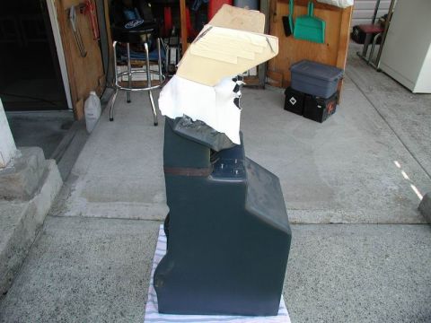 1990 Ford F-250 - A dark center console, partially covered with cardboard and white fabric, sits on a striped cloth on a concrete surface.