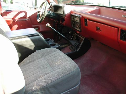 1990 Ford F-250 - The interior of a 1990 Ford F-250 shows its red dashboard, center console, and front seats.