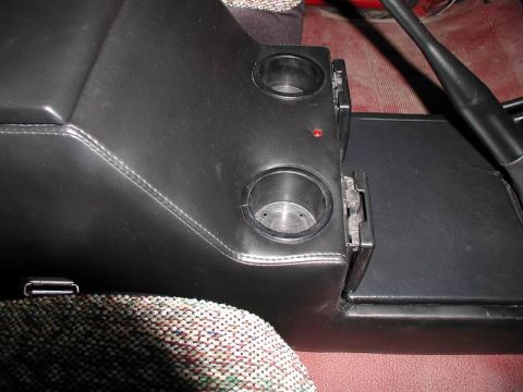 1990 Ford F-250 - This image shows a black center console with dual cup holders and a small red indicator light, likely from a vehicle's interior.