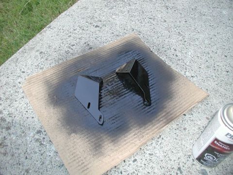 1990 Ford F-250 - Spray painting two black metal brackets outdoors on a sunny day.