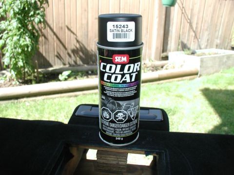 1990 Ford F-250 - A can of black spray paint is placed on a dark surface, with a wooden fence and greenery in the background.