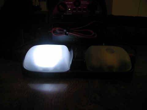 1990 Ford F-250 - A domelight assembly shows one bright white illuminated lens next to a yellowed lens, with a battery charger in the background.
