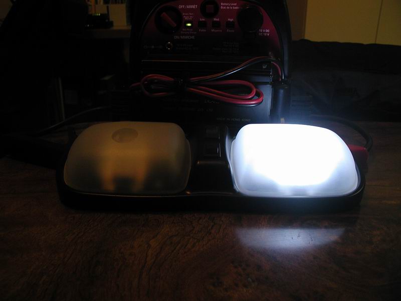 Interior dome light assembly with two lights, one illuminated white, the other dimly lit yellow, next to a battery charger