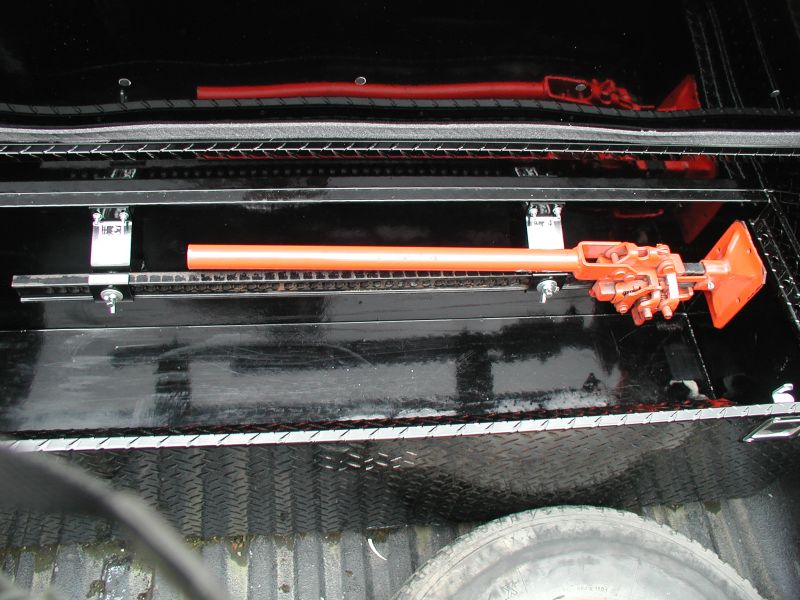 Orange Hi-Lift jack mounted on a black rack inside a truck bed