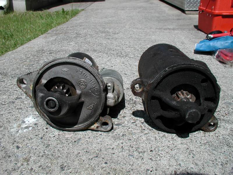 Two vehicle starters, one cleaner than the other, sit on a concrete surface