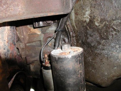 1990 Ford F-250 - Underside view of a starter motor assembly connected to the transmission housing, showing wiring and rusty components.