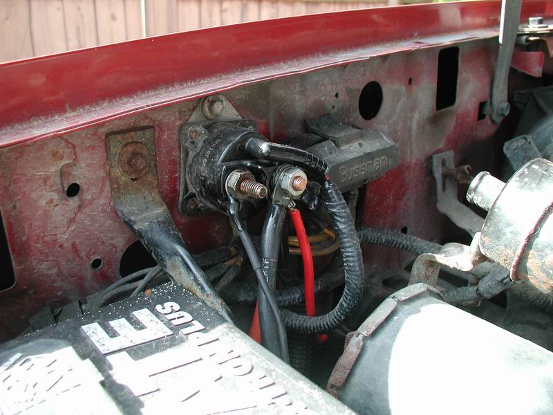 Starter relay and battery terminals on a red vehicle, with a Bussmann fuse box visible