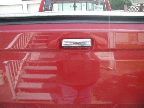 1990 Ford F-250 - Rear view of a red 1990 Ford F-250 pickup truck tailgate, showing a chrome handle and reflections.