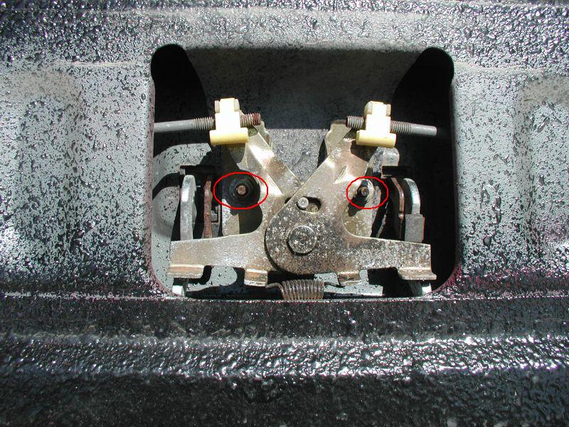 Tailgate lock mechanism with two red circles around screws. Textured black surface below