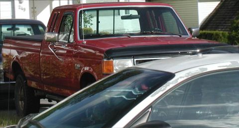 1990 Ford F-250 - A red Ford F-250 pickup truck is parked in a residential area, partially obscured by another vehicle.