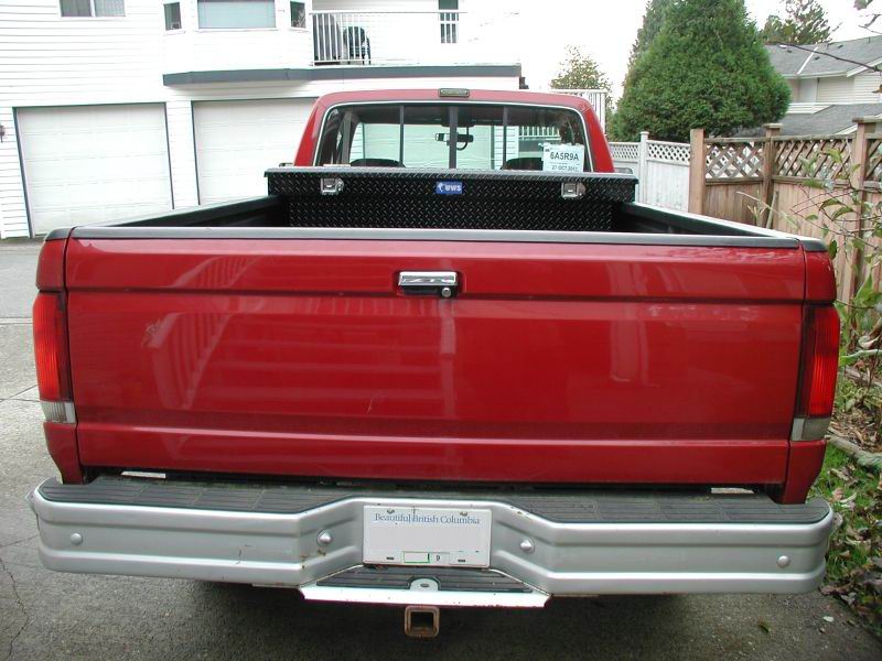 Rear view of a red Ford F-250 pickup truck with a black toolbox and a BC license plate.