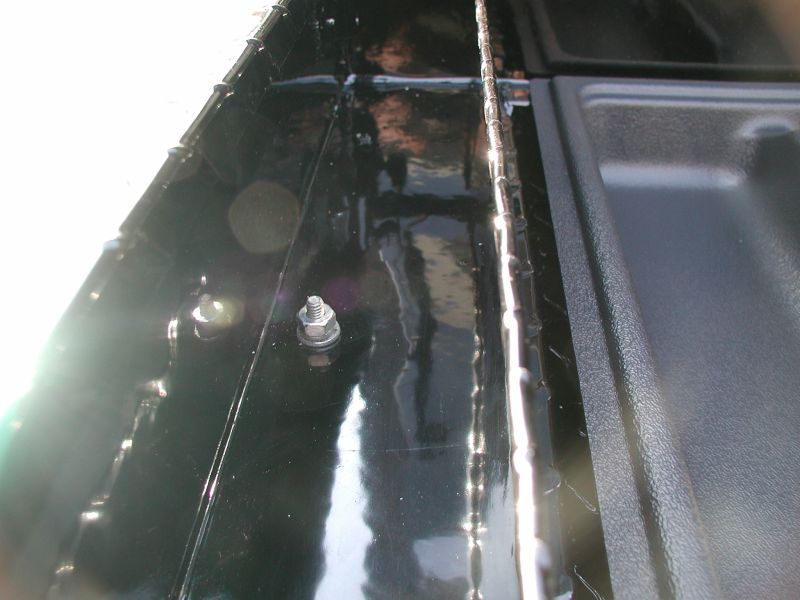 Close-up of bolt and nut inside black truck bed next to textured plastic.