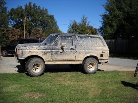 1990 Ford Bronco - Muddy 1990 Ford Bronco parked on a grassy area under a clear blue sky.