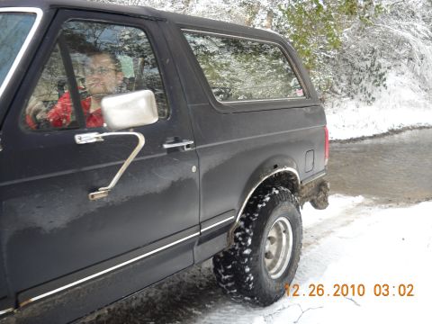 1990 Ford Bronco - A 1990 Ford Bronco is shown in a snowy outdoor setting with the driver visible through the window.