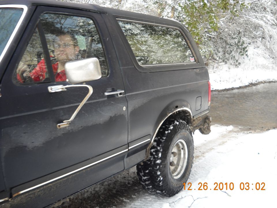 Side view of a black 1990 Ford Bronco in the snow, driver visible inside