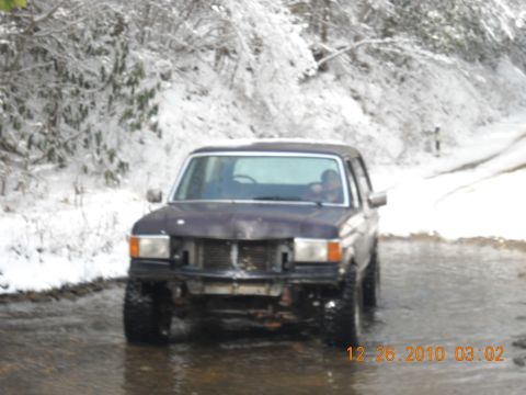 1990 Ford Bronco - A Ford Bronco navigates a snowy, wet road in this front-facing shot.