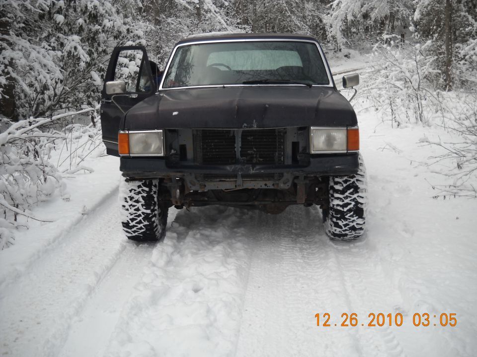 Black Ford Bronco with open driver door, off-road tires, in snowy woods