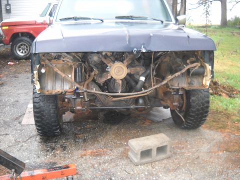 1990 Ford Bronco - The front of a 1990 Ford Bronco is shown with the grille removed, revealing the engine compartment. A red truck is parked behind it.