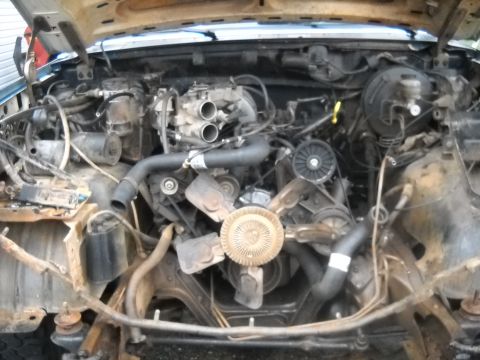 1990 Ford Bronco - The engine bay of a 1990 Ford Bronco is visible with the hood raised, revealing the engine and various mechanical parts.