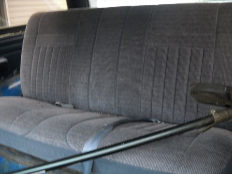 1990 Ford Bronco - The interior of a vehicle shows a gray bench seat with seatbelts and a metal bar in the foreground.