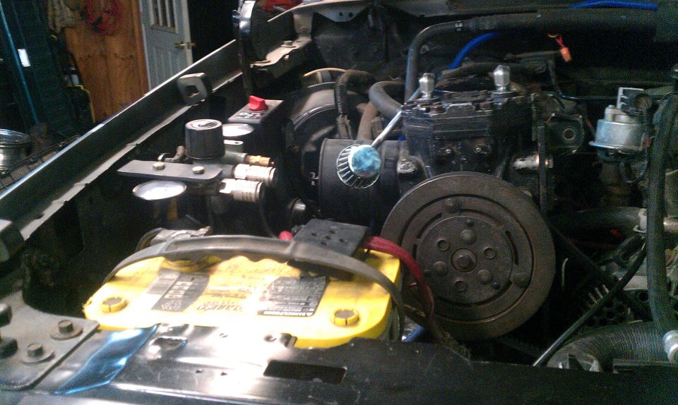 engine bay with battery, air compressor, and various hoses and components