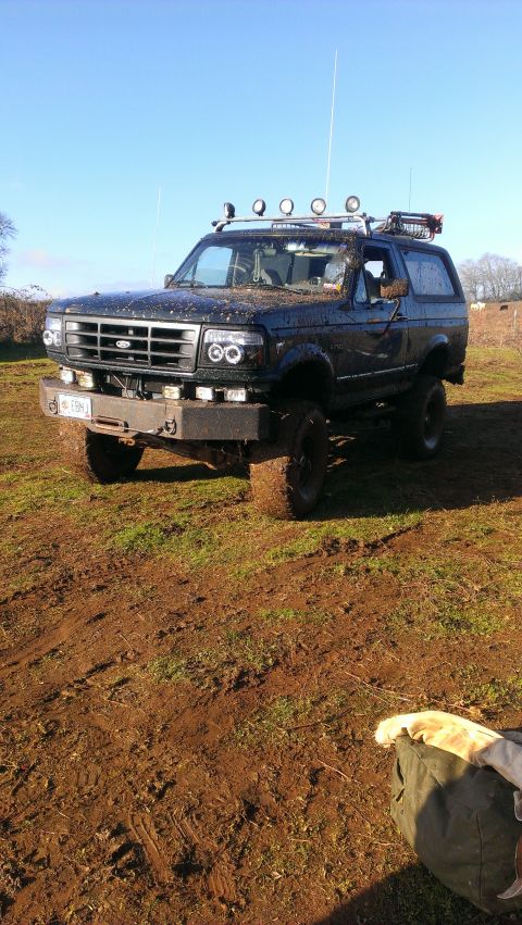 1995 Ford Bronco - A muddy Ford Bronco sits in a field under a clear blue sky, ready for off-road adventure.