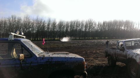 1995 Ford Bronco - Two trucks are covered in mud after driving through a wet, open field on a cloudy day.