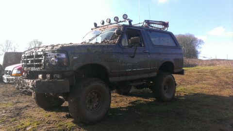 1995 Ford Bronco - This heavily mud-splattered 1995 Ford Bronco is parked in a field, equipped with a roof rack and auxiliary lights.