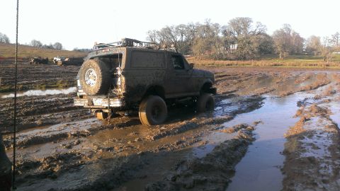 1995 Ford Bronco - This SUV is heavily covered in mud, stuck in a muddy field with a spare tire mounted on the rear.