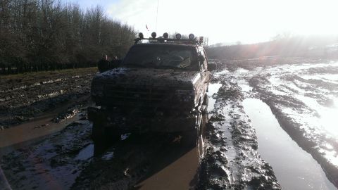 1995 Ford Bronco - SUV stuck deep in mud on a farm track, with trees lining the field.