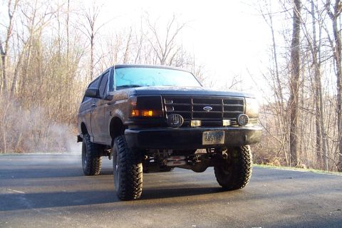 1996 Ford Bronco - Lifted 1996 Ford Bronco parked on a paved surface with trees in the background.