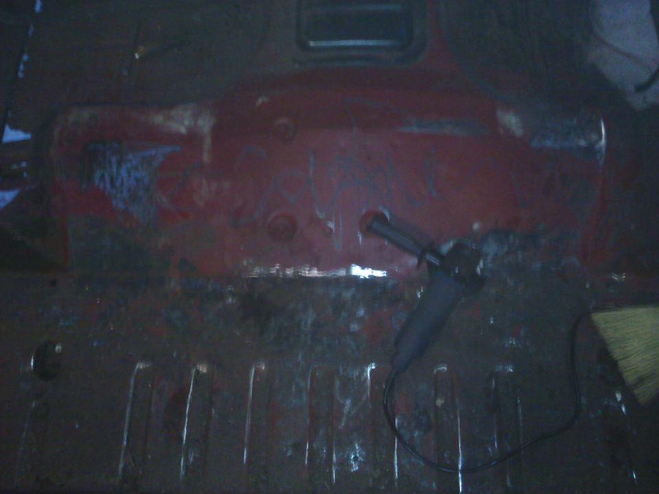 Red vehicle interior floor with rust and an angle grinder