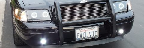 2003 Ford Crown Victoria - Frontal view of a black car equipped with a push bar, aftermarket grille, and halo headlights, a personalized license plate.