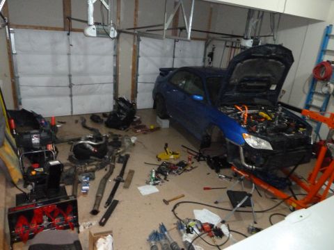 2007 Subaru Impreza - A blue 2007 Subaru Impreza is parked in a garage with its hood open, revealing the engine and surrounding disassembled parts.