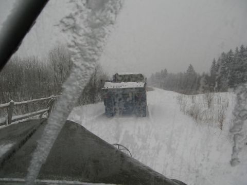 1987 Ford Bronco - Two trucks drive down a snow-covered road, viewed from inside another vehicle during a snowstorm.