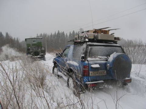 1987 Ford Bronco - Two vehicles, a blue SUV and a military truck, navigate a snowy landscape with trees in the background.