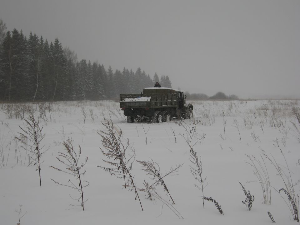 Military dump truck driving through a snowy field with trees in the background