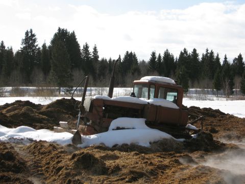 1987 Ford Bronco - An old tractor is partially buried in mud and snow with trees in the background.