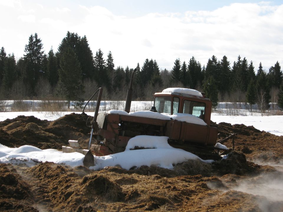old tractor stuck in mud and snow, trees in background